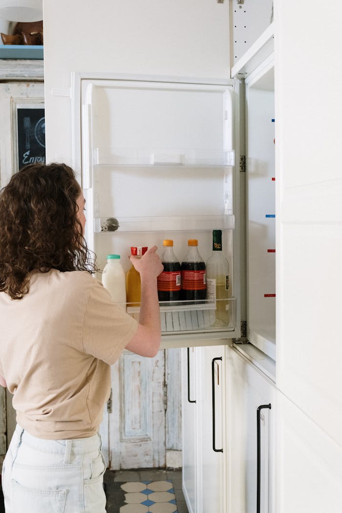 Woman with curly hair reaches for a drink in the kitchen fridge.